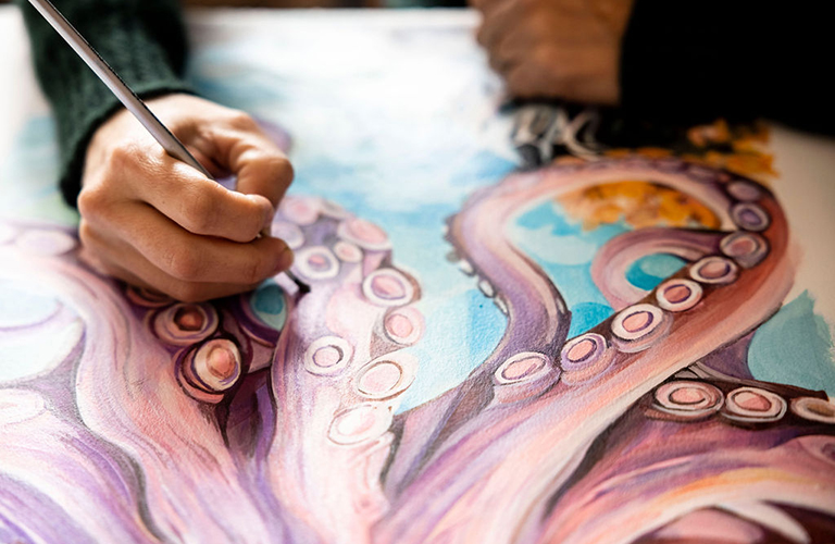 Close-up image of hands painting the legs of a purple and pink octopus 