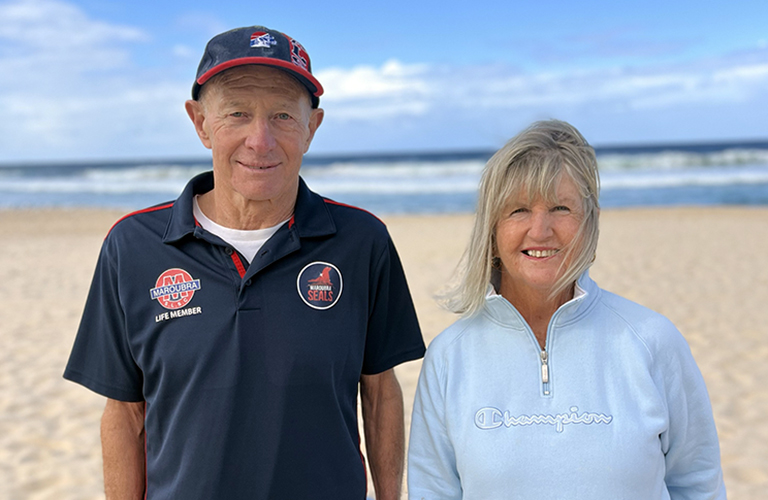 A photo of a man and woman on the beach looking at the camera and smiling