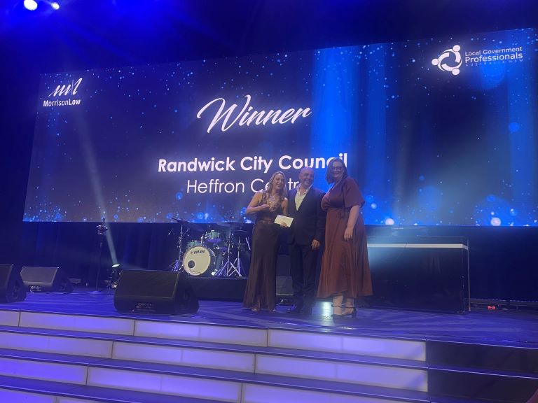 Three Council staff pose on a stage with an award. The backdrop reads Winner: Randwick City Council, Heffron Centre 